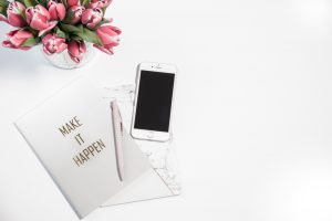 make it happen notebook and phone on white table with pink flowers