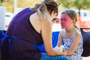 woman painting a young girls face pink as a face painting booth