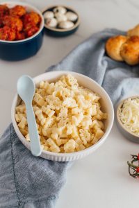 bowl of plain dinosaur pasta surrounded by sides and ingredients