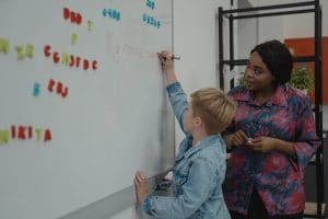 teacher helping a young student as he writes on the white board