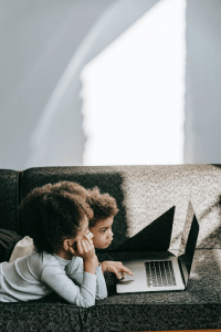 two kids lying on couch, scrolling on laptop